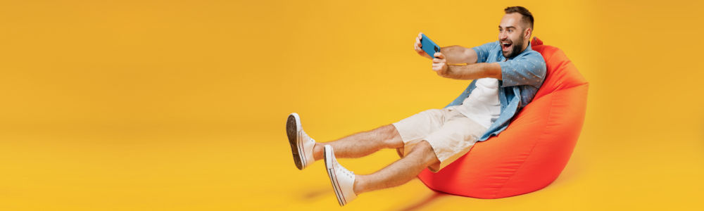 man sitting on a pillow chair celebrating a win on a game on a mobile device